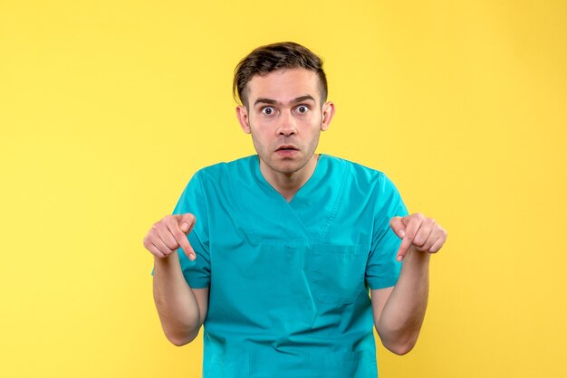 Vista frontal del médico varón sorprendido en la pared amarilla