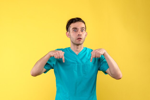 Vista frontal del médico varón sorprendido en la pared amarilla
