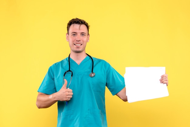 Vista frontal del médico varón sosteniendo archivos en la pared amarilla