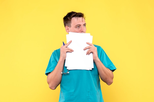Vista frontal del médico varón sosteniendo archivos en la pared amarilla