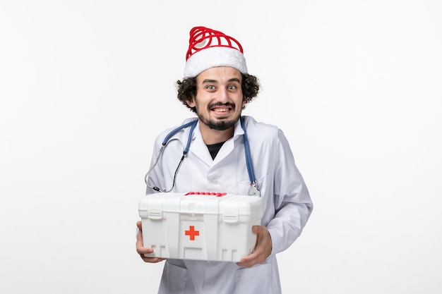 Vista frontal del médico varón sosteniendo el botiquín de primeros auxilios en la pared blanca