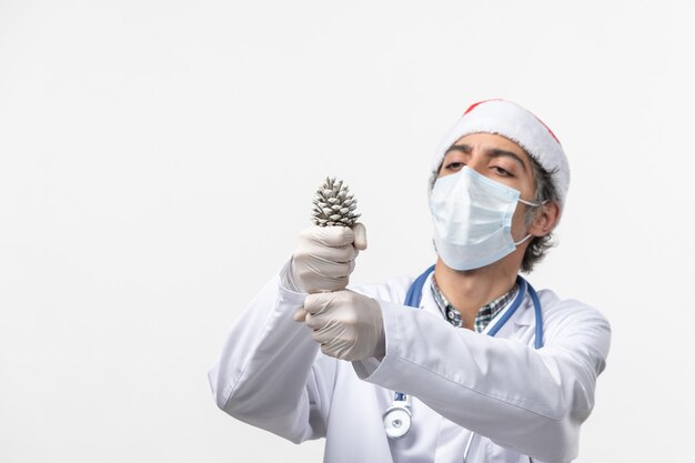 Vista frontal médico varón sosteniendo el cono en la pared blanca covid- virus de salud navideño