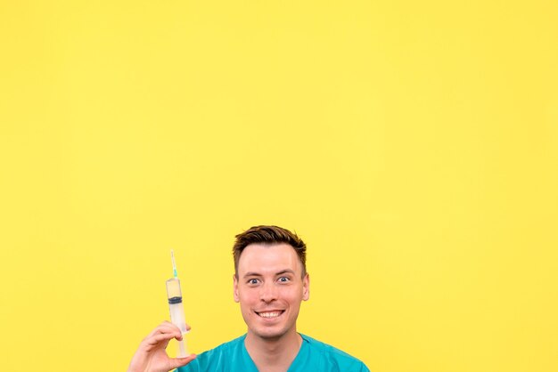 Vista frontal del médico varón sosteniendo una gran inyección en la pared amarilla