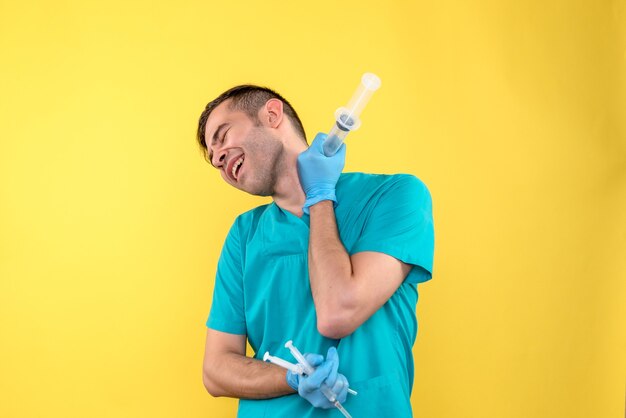 Vista frontal del médico varón sosteniendo inyecciones en pared amarilla