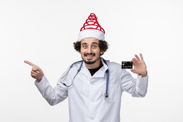 Vista frontal del médico varón sosteniendo una tarjeta bancaria en la pared blanca