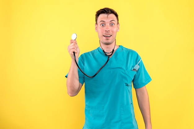 Vista frontal del médico varón sosteniendo tonómetro en pared amarilla