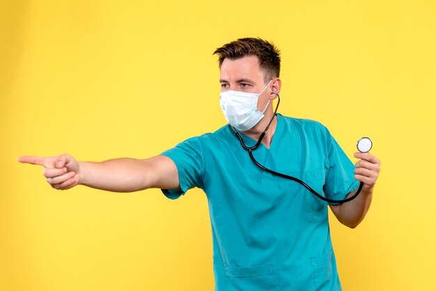 Vista frontal del médico varón con tonómetro y máscara en pared amarilla