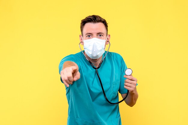 Vista frontal del médico varón con tonómetro y máscara en pared amarilla