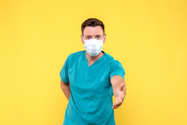 Vista frontal del médico varón tratando de darle la mano a la pared amarilla