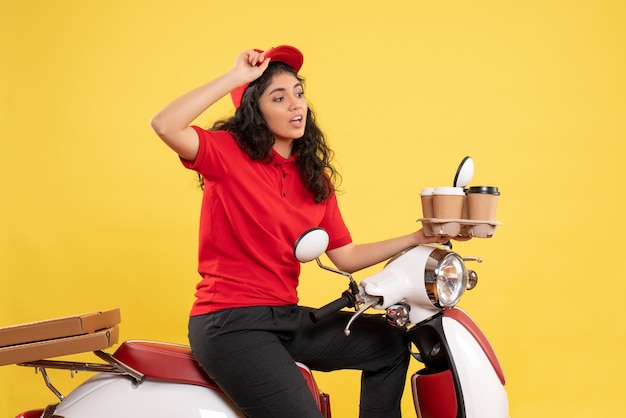 Vista frontal de mensajería femenina en bicicleta sosteniendo tazas de café sobre fondo amarillo trabajo uniforme de servicio mujer trabajo de entrega