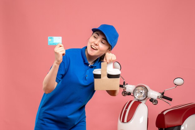 Vista frontal de mensajería femenina con café y tarjeta bancaria en rosa trabajo servicio uniforme de entrega trabajo pizza mujer bicicleta