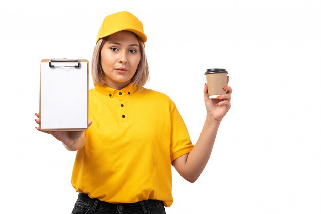 Una vista frontal de mensajería femenina en camisa amarilla gorra amarilla y jeans negros con bloc de notas y café en blanco