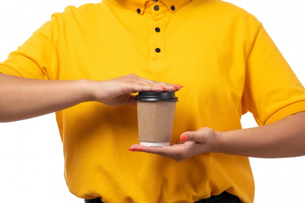 Una vista frontal de mensajería femenina en camisa amarilla gorra amarilla jeans negros con café en blanco