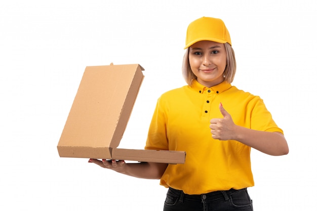 Una vista frontal de mensajería femenina en camisa amarilla gorra amarilla jeans negros con caja de pizza y sonriendo en blanco