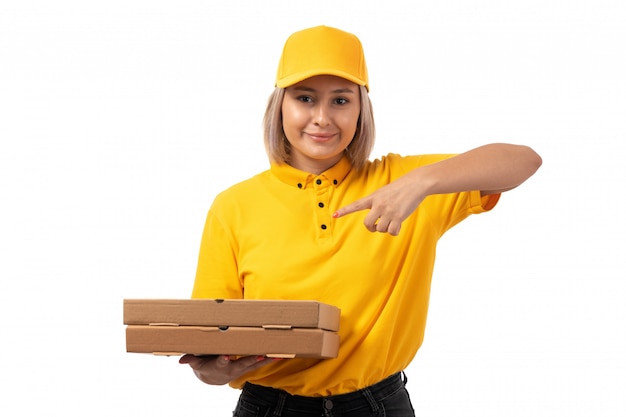 Una vista frontal de mensajería femenina en camisa amarilla gorra amarilla jeans negros con cajas de pizza sonriendo en blanco