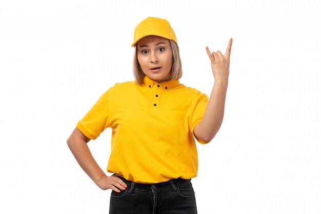 Una vista frontal de mensajería femenina en camisa amarilla gorra amarilla y jeans negros posando en estilo rockero en blanco