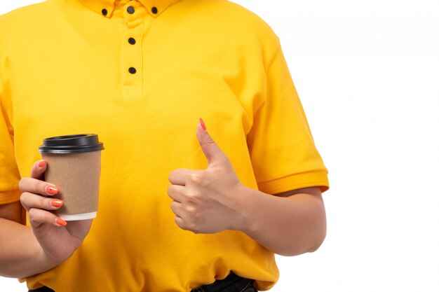Una vista frontal de mensajería femenina en camisa amarilla gorra amarilla y jeans negros posando sosteniendo café en blanco