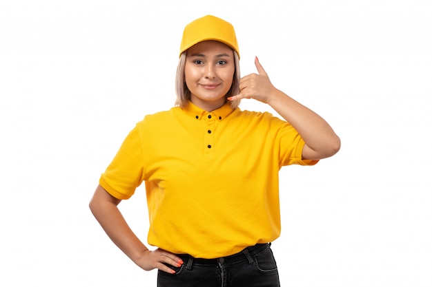 Una vista frontal de mensajería femenina en camisa amarilla gorra amarilla jeans negros sonriendo posando en blanco