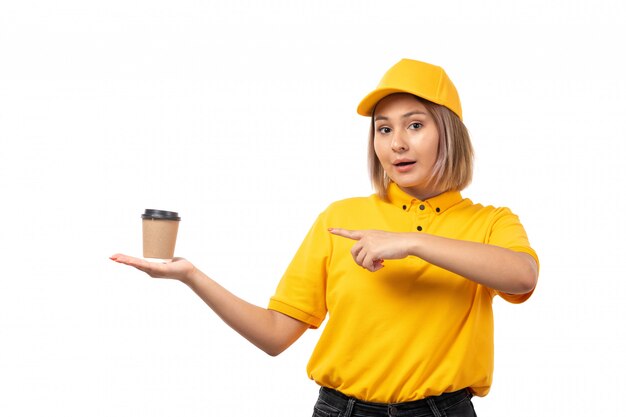 Una vista frontal de mensajería femenina en camisa amarilla gorra amarilla y jeans negros con taza de café en blanco