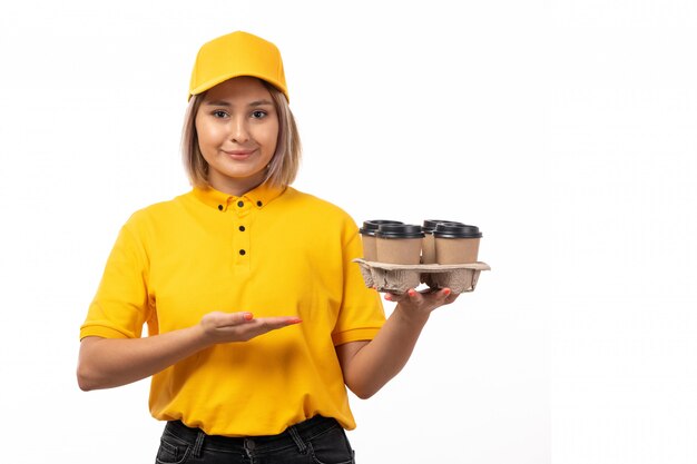 Una vista frontal de mensajería femenina en camisa amarilla gorra amarilla y jeans negros con tazas de café en blanco