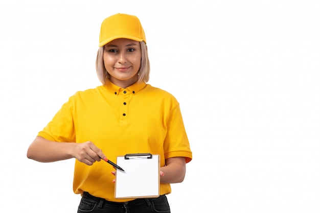 Una vista frontal de mensajería femenina en camisa amarilla gorra amarilla con papel y bolígrafo sonriendo en blanco