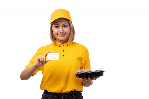 Una vista frontal de mensajería femenina en camisa amarilla gorra amarilla sonriendo sosteniendo la tarjeta blanca sobre blanco