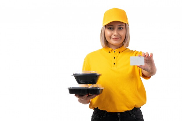 Una vista frontal de mensajería femenina en camisa amarilla y gorra amarilla sosteniendo cuencos con comida y tarjeta blanca en el blanco