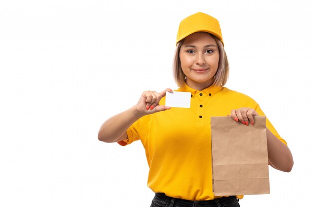 Una vista frontal de mensajería femenina en camisa amarilla y gorra amarilla sosteniendo cuencos con comida y tarjeta blanca sobre blanco