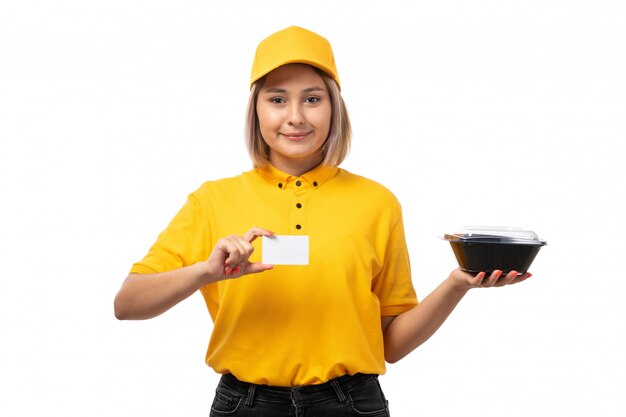 Una vista frontal de mensajería femenina en camisa amarilla gorra amarilla con tarjeta blanca y cuencos con comida sonriendo en blanco