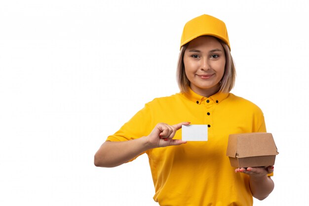 Una vista frontal de mensajería femenina en camisa amarilla gorra amarilla con tarjeta blanca pequeña caja sonriendo en blanco