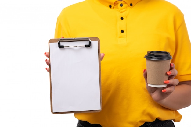 Foto gratuita una vista frontal de mensajería femenina en camisa amarilla jeans negros con bloc de notas y una taza de café en blanco