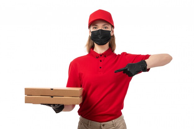 Una vista frontal de mensajería femenina en camisa roja capblack guantes rojos y máscara negra con cajas de pizza en blanco