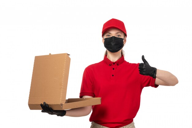 Una vista frontal de mensajería femenina en camisa roja gorra roja guantes negros y máscara negra con caja de pizza en blanco