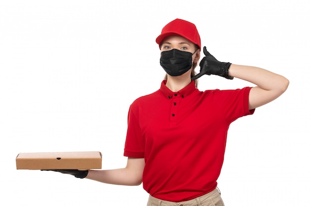Una vista frontal de mensajería femenina en camisa roja gorra roja guantes negros y máscara negra con caja de pizza posando en blanco