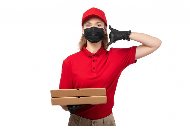 Una vista frontal de mensajería femenina en camisa roja gorra roja guantes negros y máscara negra con cajas de pizza en blanco