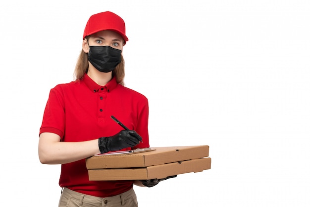 Una vista frontal de mensajería femenina en camisa roja gorra roja guantes negros y máscara negra con cajas de pizza y escribir órdenes en blanco