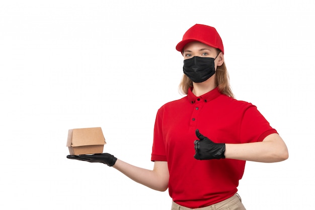 Una vista frontal de mensajería femenina en camisa roja gorra roja guantes negros y máscara negra con paquetes de alimentos en blanco