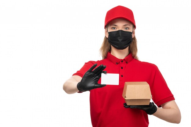 Una vista frontal de mensajería femenina en camisa roja gorra roja y máscara negra con tarjeta blanca y paquete con comida