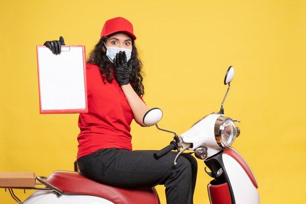 Vista frontal de mensajería femenina en máscara sosteniendo la nota de archivo sobre fondo amarillo covid- trabajo servicio uniforme trabajo entrega pandemia