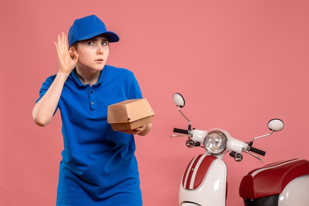 Vista frontal de mensajería femenina con pequeño paquete de comida escuchando en rosa trabajo servicio uniforme de entrega de trabajo bicicleta trabajador pizza mujer