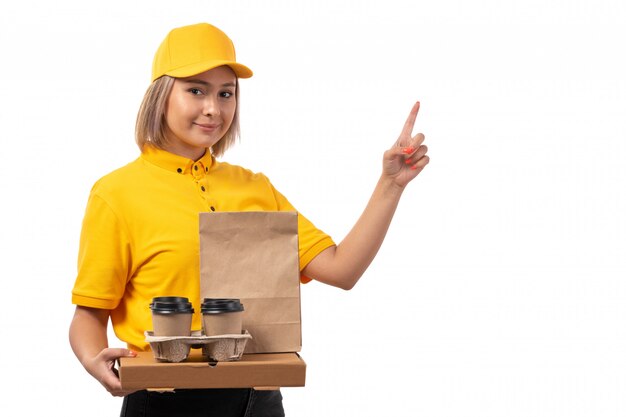 Una vista frontal de mensajería femenina en la tapa amarilla camisa amarilla con caja de pizza café sonriendo en blanco