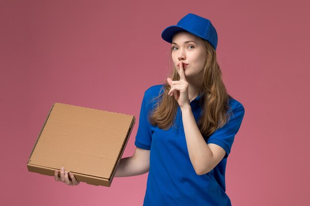 Vista frontal de mensajería femenina en uniforme azul con caja de comida que muestra el signo de silencio sobre fondo rosa empresa uniforme de servicio de trabajo