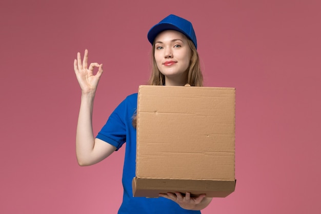 Vista frontal de mensajería femenina en uniforme azul con caja de entrega de alimentos sonriendo sobre fondo rosa empresa uniforme de servicio de trabajo