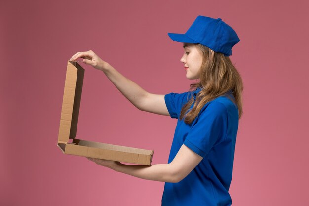 Vista frontal de mensajería femenina en uniforme azul sosteniendo la caja de comida abriéndola en la empresa de uniforme de servicio de trabajador de trabajo de escritorio rosa