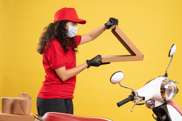 Vista frontal de mensajería femenina en uniforme rojo con caja de pizza sobre fondo amarillo trabajador entrega covid- servicio virus trabajo