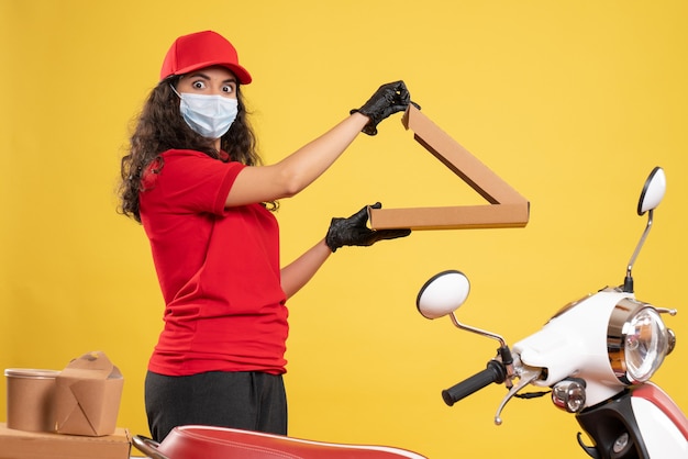 Vista frontal de mensajería femenina en uniforme rojo con caja de pizza sobre fondo amarillo trabajador entrega covid- trabajo de virus de servicio pandémico