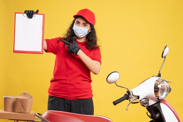 Vista frontal de mensajería femenina en uniforme rojo con nota de archivo sobre fondo amarillo entrega covid- servicio uniforme pandemia trabajo