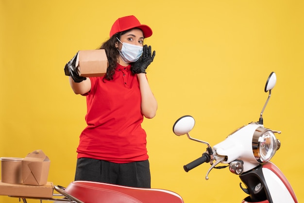 Vista frontal de mensajería femenina en uniforme rojo sosteniendo un pequeño paquete de comida sobre fondo amarillo pandemia de trabajador de entrega de servicio de trabajo covid