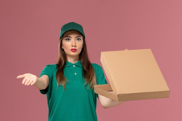 Vista frontal de mensajería femenina en uniforme verde con caja de entrega de alimentos en la pared rosa empresa servicio de trabajo uniforme entrega de trabajo