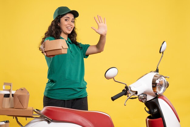 Vista frontal de mensajería femenina en uniforme verde con pequeño paquete de comida sobre fondo amarillo trabajo color trabajo entrega mujer servicio trabajador comida